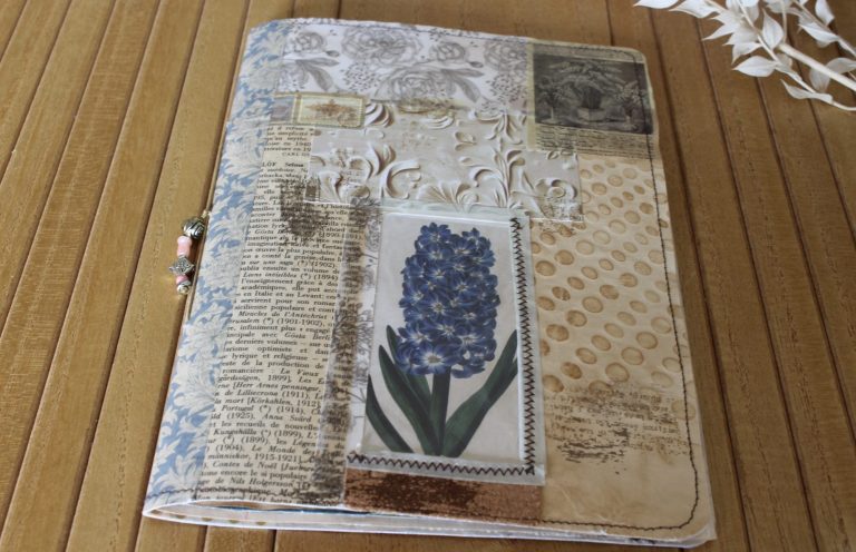 Junk journal fermé, couverture en collage de papiers anciens avec une jacinthe bleue, sur un plateau en bois