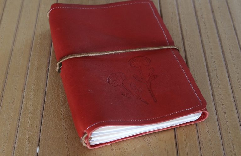 Carnet rechargeable en cuir rouge fermé par un élastique, avec ses cahiers visibles

