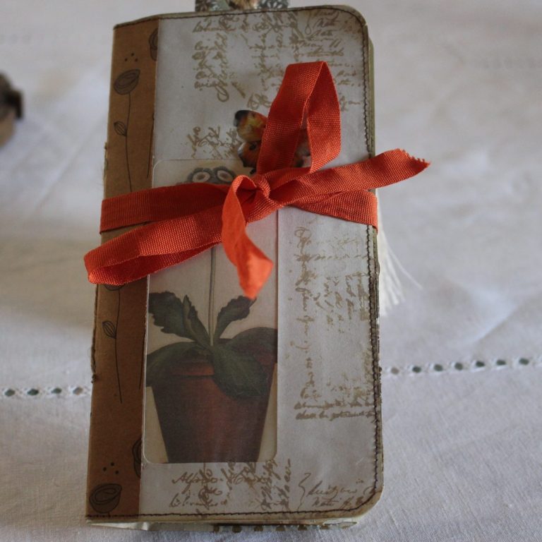 carnet fait main Carnet fermé noué d'un ruban rouge, orné d'un papillon et d'un motif de pot de plante, posé sur un tissu clair